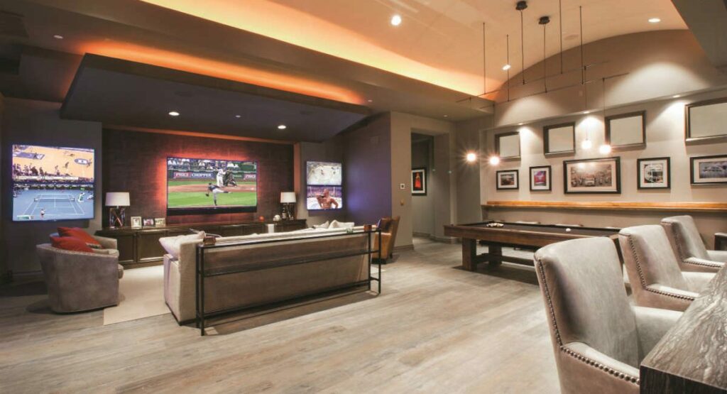 Texas Longhorns themed entertainment system in basement level of house. Burnt orange lighting, five displays arranged on wall.