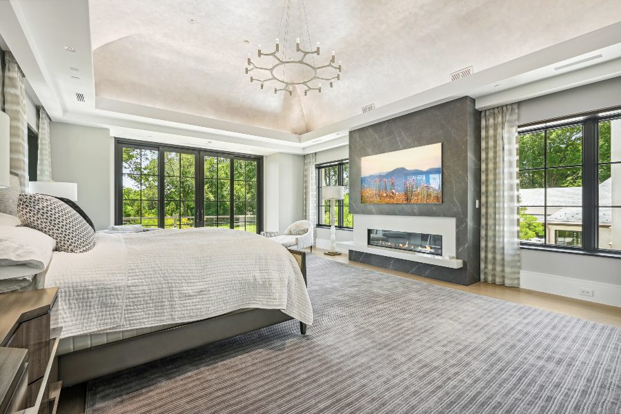 Bedroom area, high arching ceilings with ample natural lighting surrounding a central propane fireplace with gray marble and mounted digital artwork TV