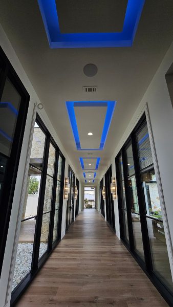 Small hallway leading through bright natural lighting with blue linear lighting in coved recesses overhead Elite AV and Lighting