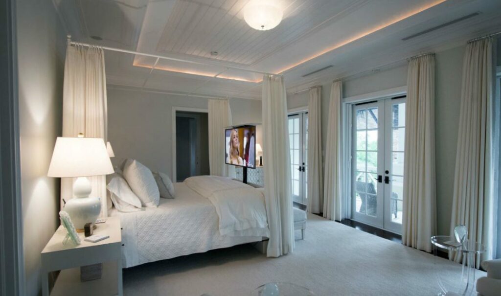 Interior white bedroom with motorized TV lift rising out of bed.
