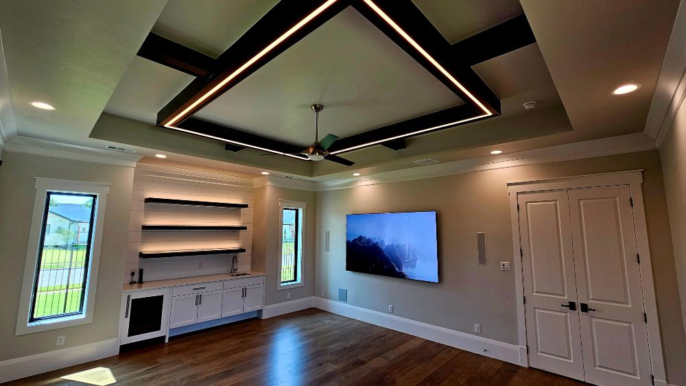 Living area with floating illuminated shelving, wall-mounted TV and overhead access lighting.