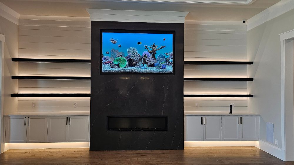 Interior forward shot of TV mounted over black marble, black glass fireplace with floating illuminated shelves of ample accent lighting, Elite AVL