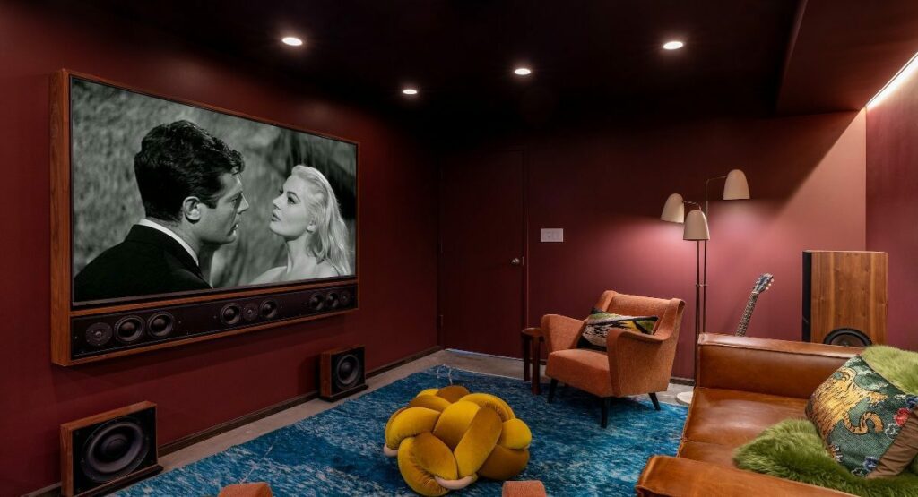 Stylish retro screening room with framed television and speaker system mounted on wall playing classic black and white movie.