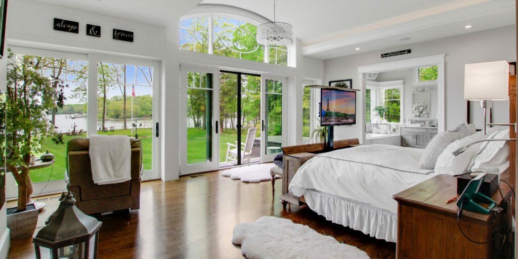 Motorized TV lift embedded in cabinet in modern bedroom overlooking lawn and lake.